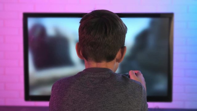 Rear view of a little boy playing shooter video game at his computer