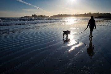 A woman walks her dog along a beach at sunset in Tofino, British Columbia