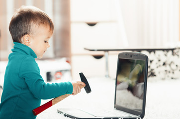 a little boy with a hammer smashes the laptop