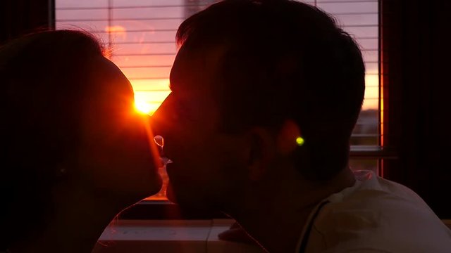 A man and woman in love kiss at home against the window and on a beautiful fiery sunset. slowmotion, HD, 1920x1080