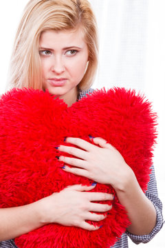 Sad woman holding red pillow in heart shape