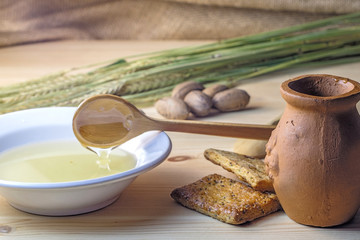 wooden spoon in a bowl of honey, a clay pot on a wooden table