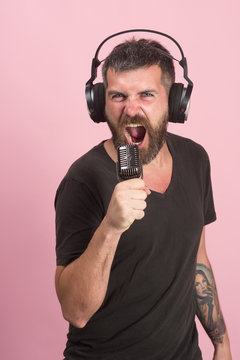 Man sings on pink background. Dj with beard wears headphones.