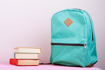 Blue school backpack and books is on a pink wooden table on pink background