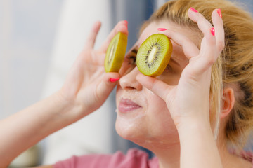 Woman having gel mask on face holding kiwi