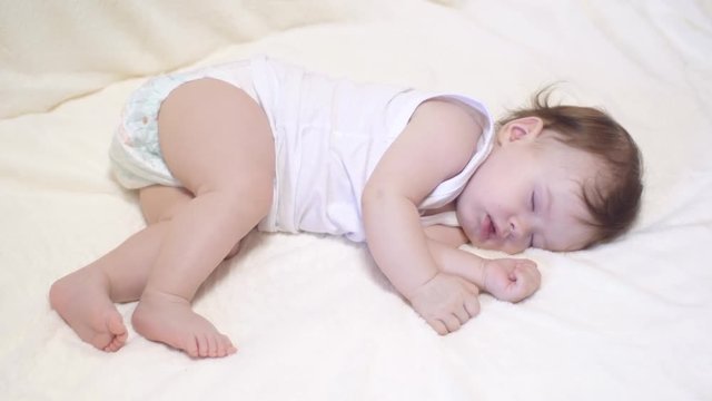 Small baby sleeps in his crib on white blanket.