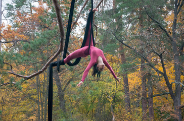 Woman dancing with aerial silk on a trees background.