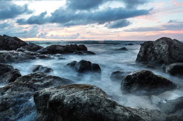 Fototapeta na wymiar Waves in long exposure in the ocean at sunset at Koh Lanta with Stones in the sea and Phi Phi islands in the horizon, Koh Lanta, Thailand, Asia