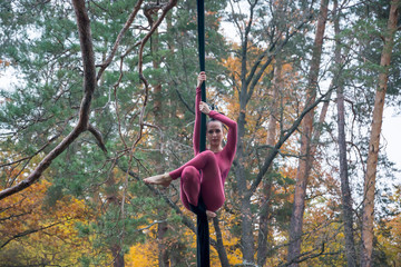 Woman dancing with aerial silk on a trees background.