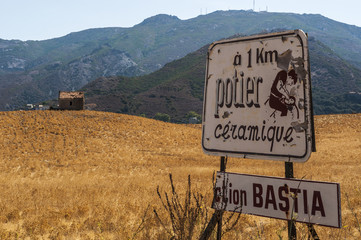 Corsica, 28/08/2017: il cartello di un laboratorio di ceramica artigianale in un campo di grano nella campagna di Patrimonio, borgo dell'Alta Corsica circondato da colline verdi e vigneti
