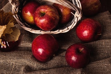 Autumn composition with fresh red apples in a wooden basket on rustic wooden background. Red apples on linen background