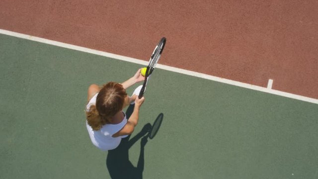  Female tennis player throws ball into the air to serve. Overhead view slowmo