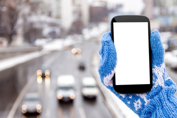 Female / woman / girl hand in blue mittens with mockup smartphone in winter in urban scene