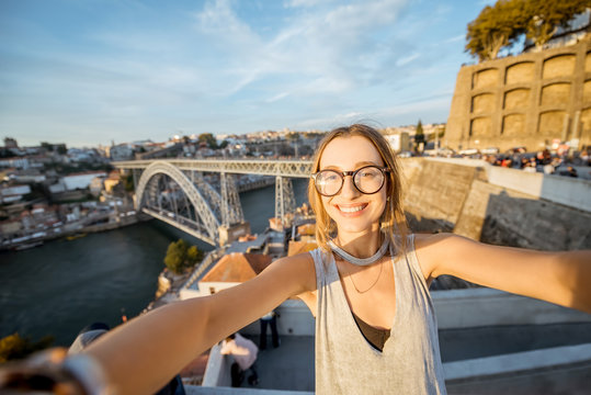 Young woman tourist making selfie photo on the beautiful cityscape background during the sunset in Porto city, Portugal