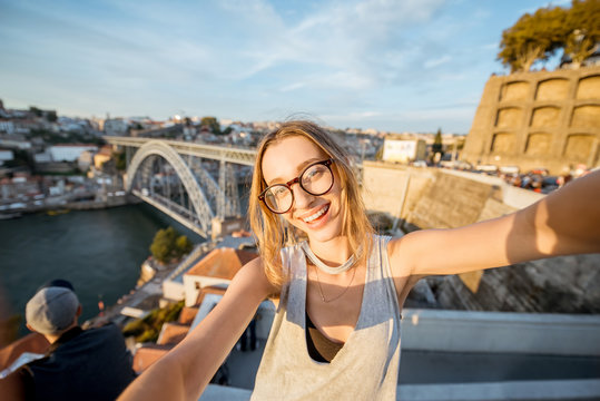 Young woman tourist making selfie photo on the beautiful cityscape background during the sunset in Porto city, Portugal