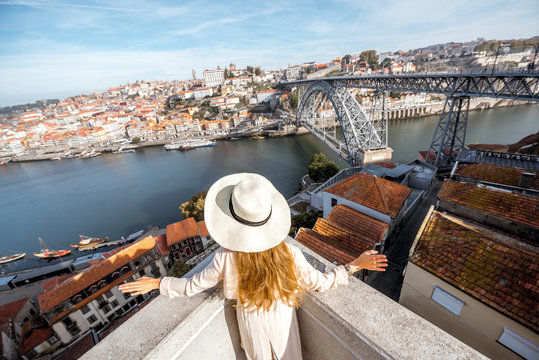 Young woman traveler in sunhat enjoying beautiful aerial cityscape view with Douro river and Luise bridge during the morning light in Porto, Portugal