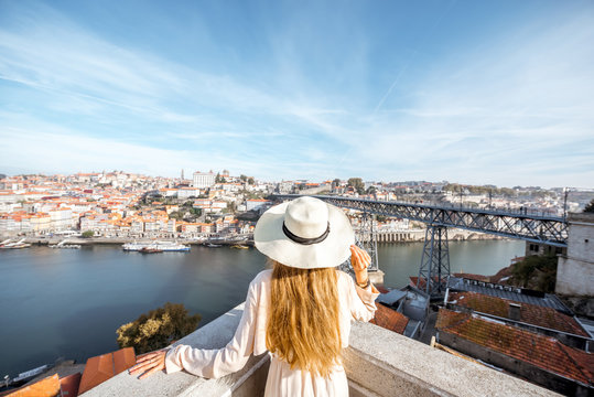 Young woman traveler in sunhat standing back on the beautiful aerial cityscape background with Douro river and Luise bridge during the morning light in Porto, Portugal