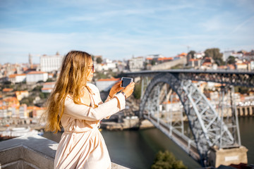 Young woman photographing with phone beautiful cityscape view with famous iron bridge in Porto...
