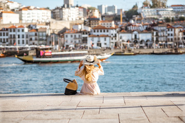Young woman tourist sitting back on the Ribeira promenade enjoying cityscape view on the Porto city during the sunny day in Portugal