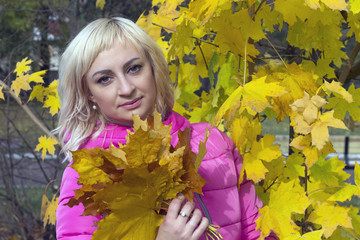 Beautiful girl, blonde, under a tree with a bouquet of maple leaves