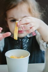 Little girl eating french fries on restaurant.