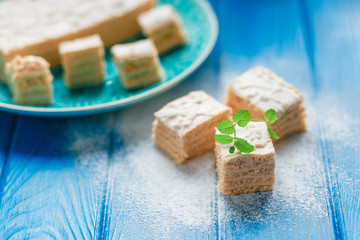 Biscuit cake pie apple candy pastila, mint leaves on blue wood cutting board background. Small square pieces paste