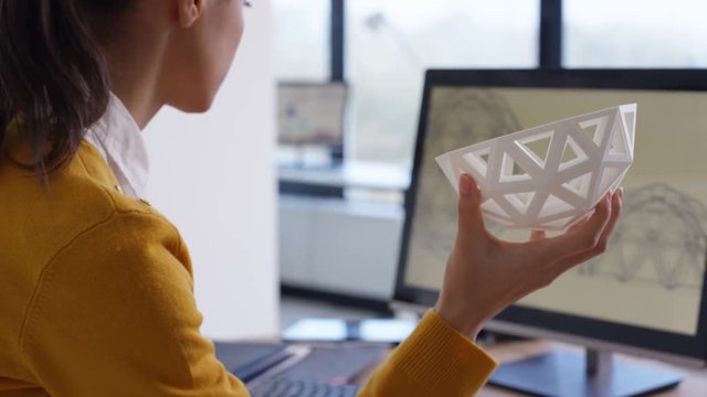  Designer working at her desk looking at 3D printed object