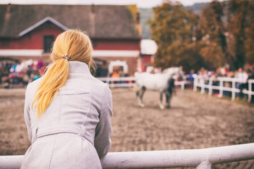 Blonde woman is watching a horse auction, English thoroughbred on a show - obrazy, fototapety, plakaty