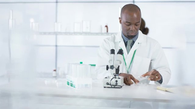  Research scientist working in laboratory, looking at sample under microscope.