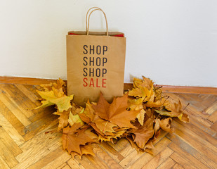 Sale sign on a shopping bag surrounded with yellow leaves on a wooden floor