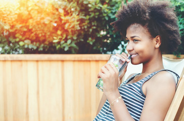 Squinting black girl with glass of drink outdoor