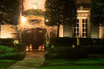 Fotobehang Het huis is versierd voor Halloween: de ingang van het huis is strakgetrokken met spinnenwebben, pompoenen met uitgesneden mokken en gloeit van binnenuit. Nacht © Irina K.