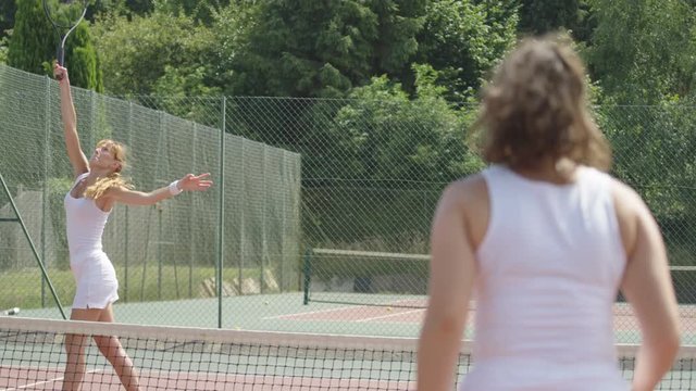  Competitive female tennis player playing against opponent on outdoor court