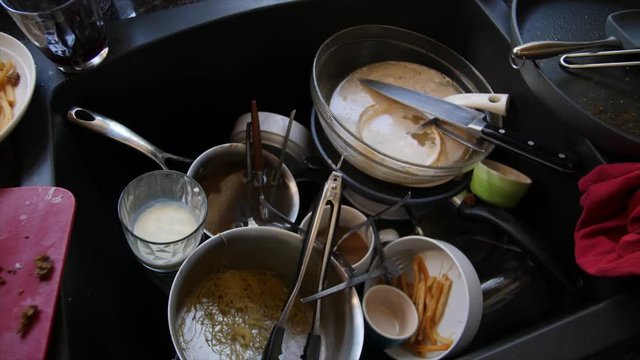 ADDING TO THE DIRTY DISHES IN THE KITCHEN SINK.  Slow dolly shot.