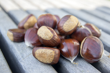 Raw sweet chestnuts scattered on a wooden table, tasty and healthy brownish nuts