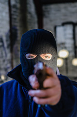 Man/terrorist wearing a black balaclava, pointing a handgun at the viewer - obrazy, fototapety, plakaty