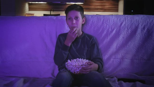 Little boy watching a movie on on TV and eating popcorn