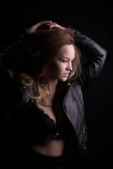 Dramatic portrait of young model with lush blonde hair, wears leather jacket, posing with shadow on her face