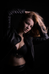 Sexy young model with lush blonde hair, wears leather jacket and lace bra, posing with shadow on her face