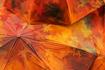 Fall abstract grunge background texture from red colored umbrellas with maple leaves. Autumn light and colors