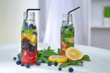 Bottles of infused water with fruits and berries on table