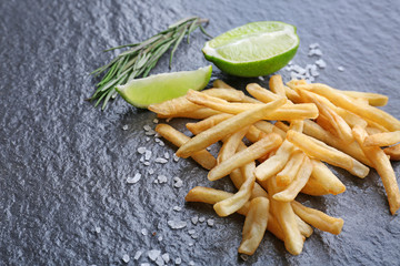 Yummy french fries with lime slices on dark texture background