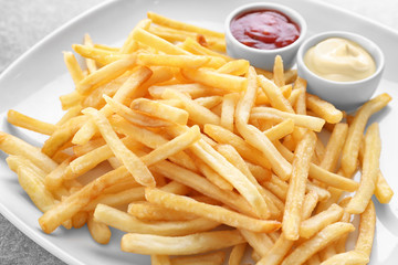 Plate with yummy french fries and sauces in small bowls on table