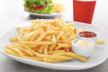 Plate with yummy french fries and sauces in small bowls on table