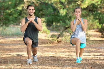 Young man and woman doing exercises in park