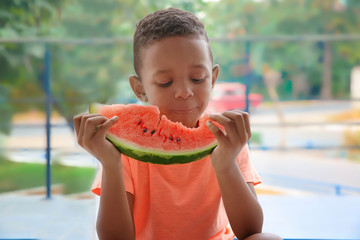 Cute African American boy eating watermelon at home