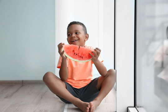 Cute African American boy eating watermelon at home
