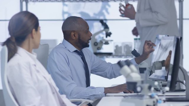  Medical researchers in the lab, working on computers & discussing their work.