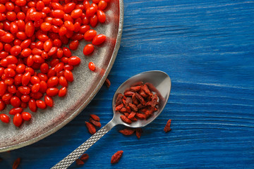 Plate and spoon with goji berries on wooden background