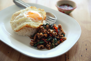 stir fried pork and basil with rice and egg on wood background thai food
